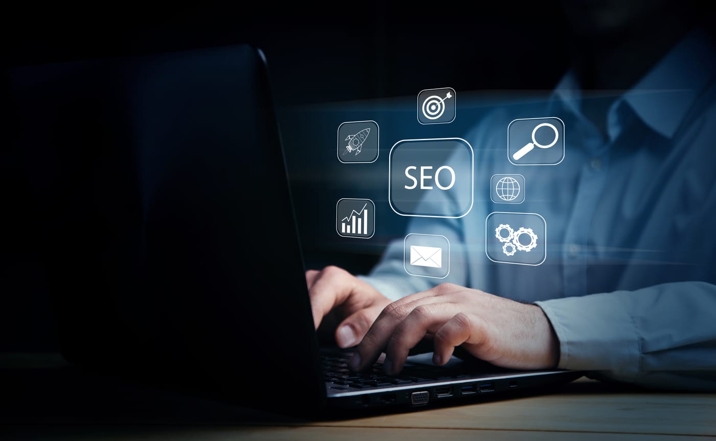 Mains tapant sur un ordinateur portable avec des icônes numériques lumineuses de SEO, marketing et analyse flottant au-dessus